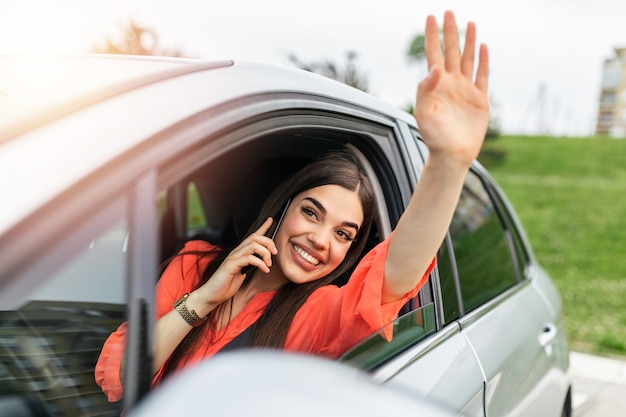 Young woman talking on the phone in the car and waving.