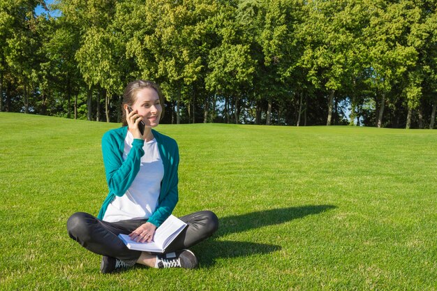 Young woman talking on the phone in the park on the green grass against the background of trees