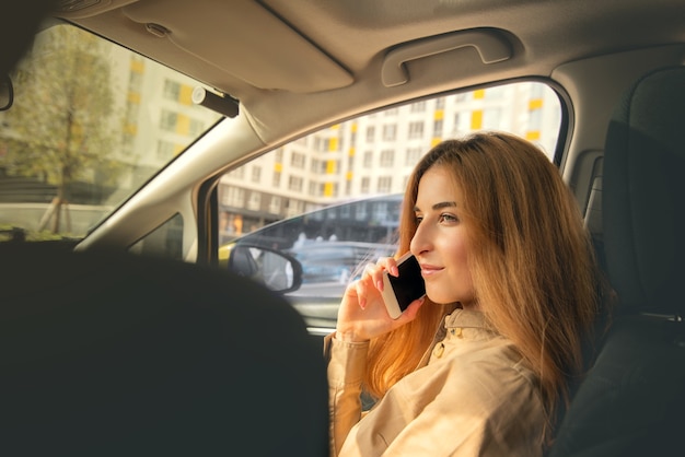 Молодая женщина разговаривает по телефону, сидя на переднем пассажирском сиденье автомобиля