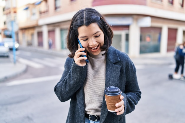 Молодая женщина разговаривает по смартфону и пьет кофе на улице