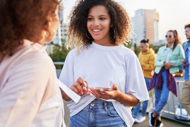 Young woman talking together outdoors and people in the background