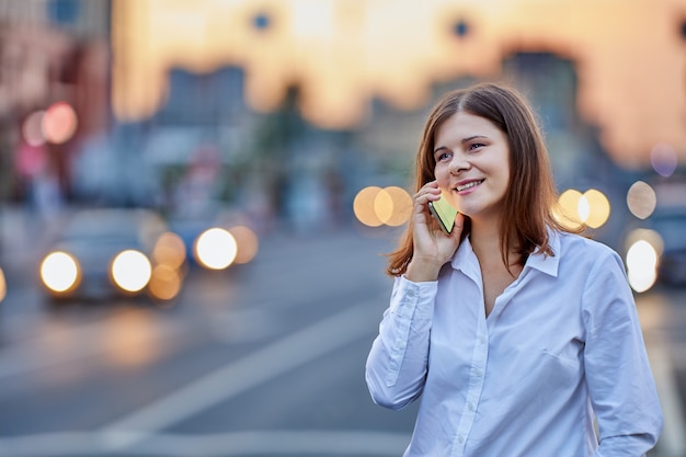 Young woman talks by smartphone near traffic