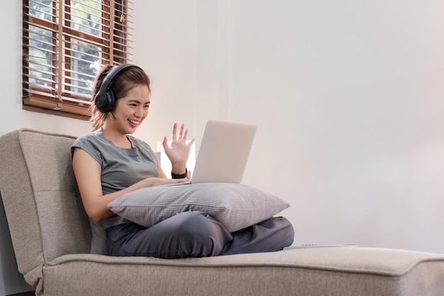 한 젊은 여성 이 거실 에 있는 노트북 에서 비디오 통화 프로그램 을 통해 친구 와 대화 하고 있다