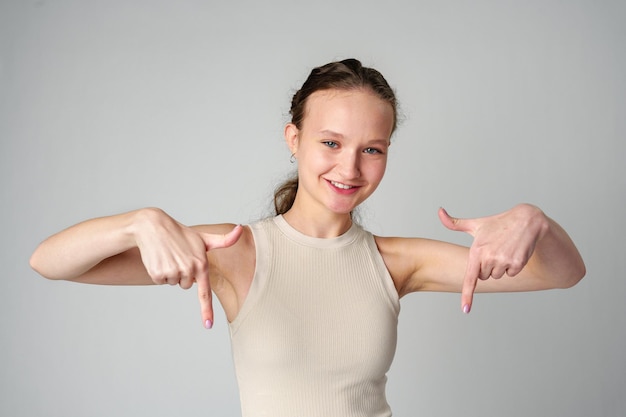 Photo young woman in tank top pointing down in studio