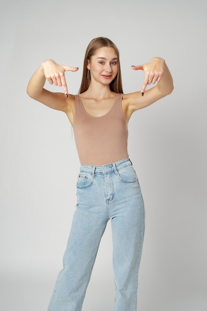 Photo young woman in tank top pointing at something on gray background