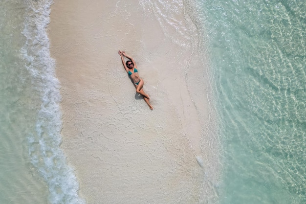 Photo young woman tanning sunbathing woman wearing bikini at the beach on a white sand from above view from drone