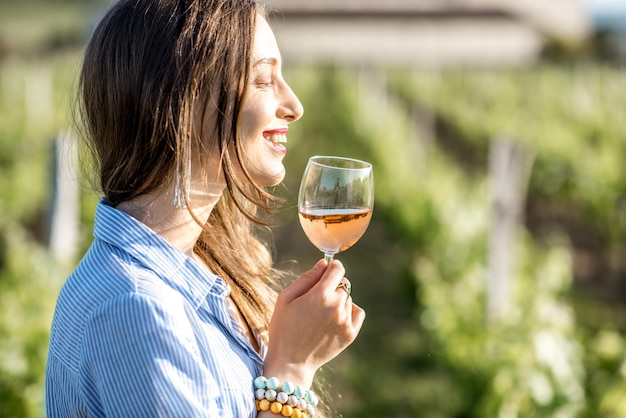 Young woman tasting wine standing outdoors on the vineyard in bordeaux region during the sunset in france