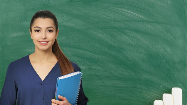 young woman teacher holding notebooks with smiling face with greenish background