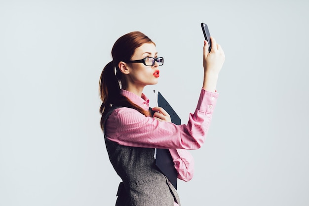 Young woman teacher with red hair in glasses holds a phone in her hand, lifted the phone upwards