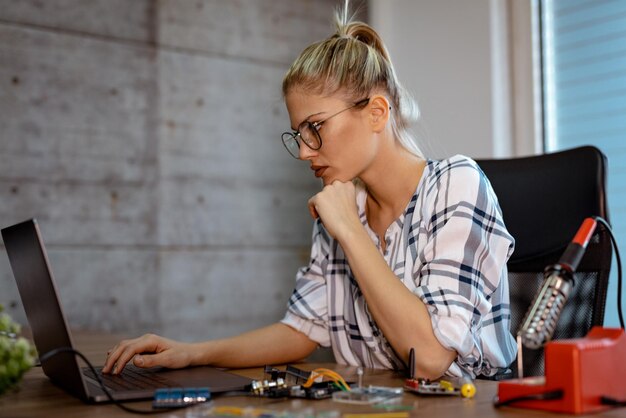 Photo young woman technician focused on the repair of electronic equipment cecking something on the laptop.