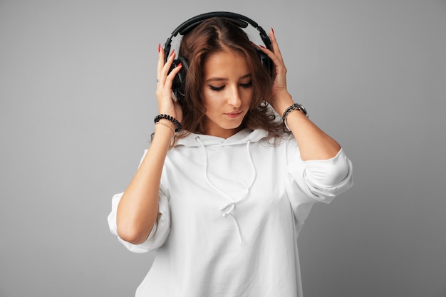 Young woman teenager listening to music with her headphones over a grey background 