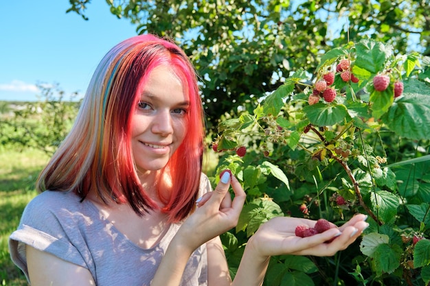 Молодая женщина-подросток собирает с куста спелую красную малину
