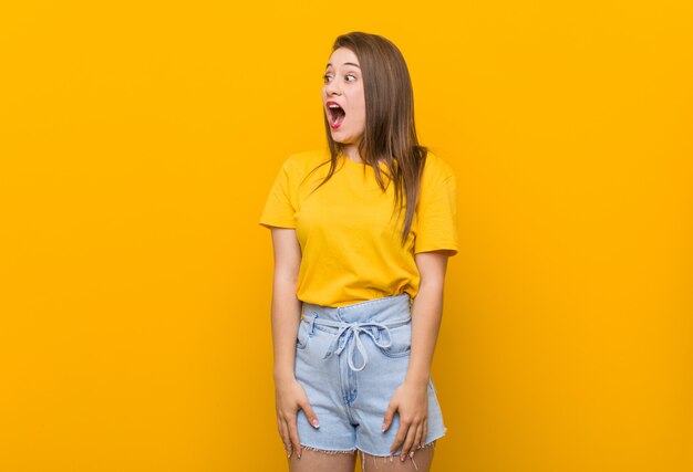 Young woman teenager wearing a yellow shirt being shocked because of something she has seen.