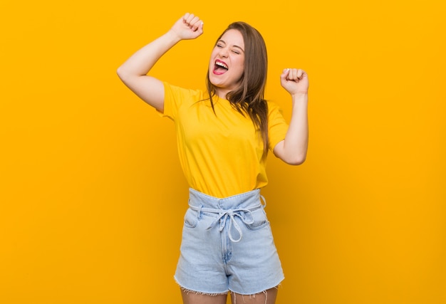 特別な日を祝う黄色いシャツを着た若い女性のティーンエイジャーは、エネルギーでジャンプして腕を上げます。