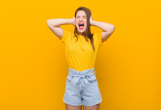 Young woman teenager wearing a yellow shirt covering ears with hands trying not to hear too loud sound.