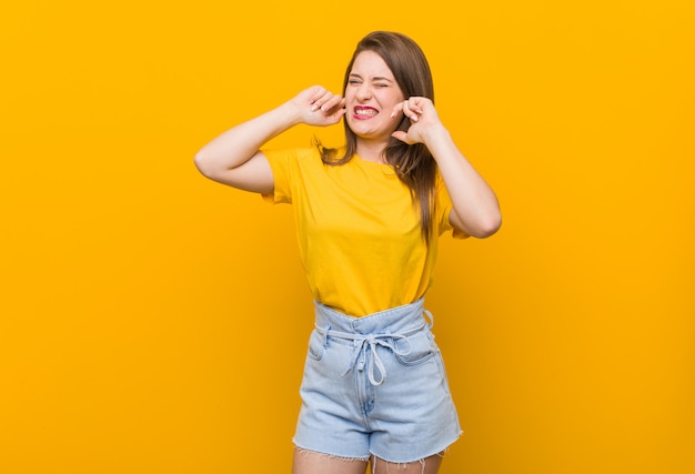 Young woman teenager wearing a yellow shirt covering ears with hands.