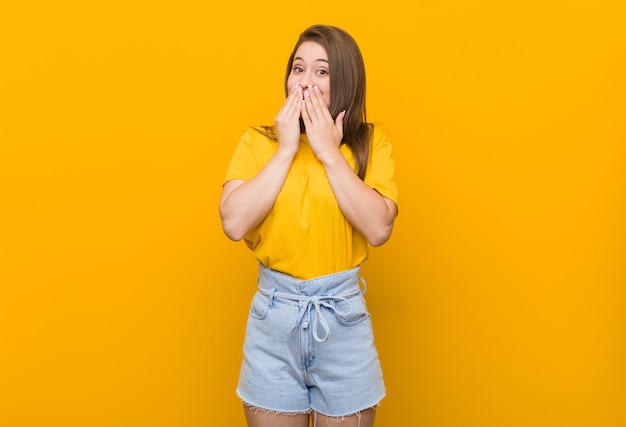 Young woman teenager wearing a yellow shirt laughing about something, covering mouth with hands.