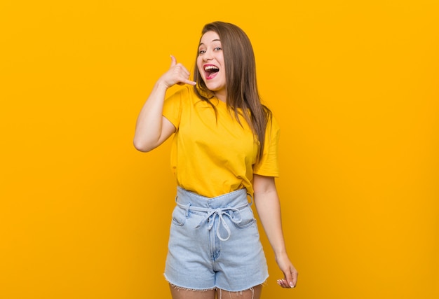 Young woman teenager wearing a yellow shirt showing a mobile phone call gesture with fingers.