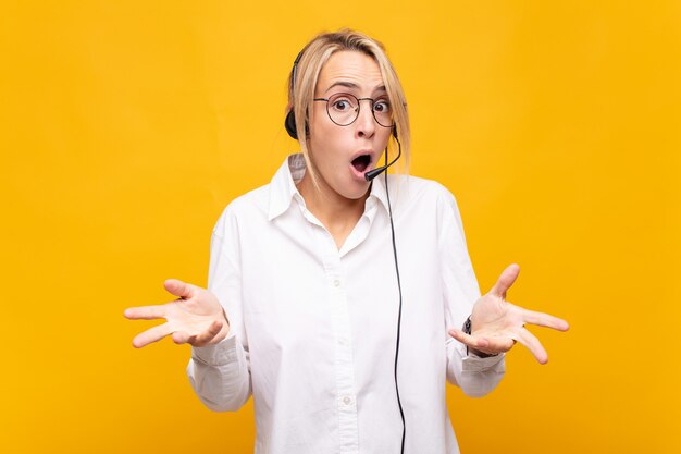 Young woman telemarketer feeling extremely shocked and surprised, anxious and panicking, with a stressed and horrified look