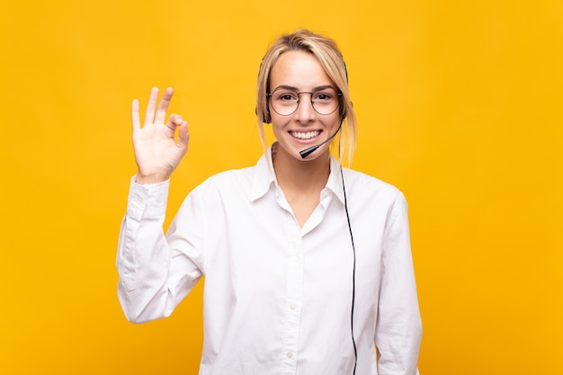 Young woman telemarketer feeling happy, relaxed and satisfied, showing approval with okay gesture, smiling