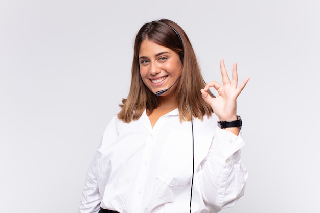 Young woman telemarketer feeling happy, relaxed and satisfied, showing approval with okay gesture, smiling