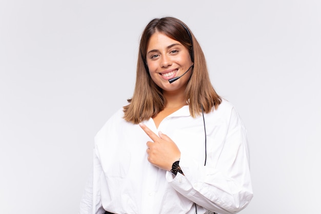 Young woman telemarketer smiling cheerfully, feeling happy and pointing to the side and upwards, showing object in copy space