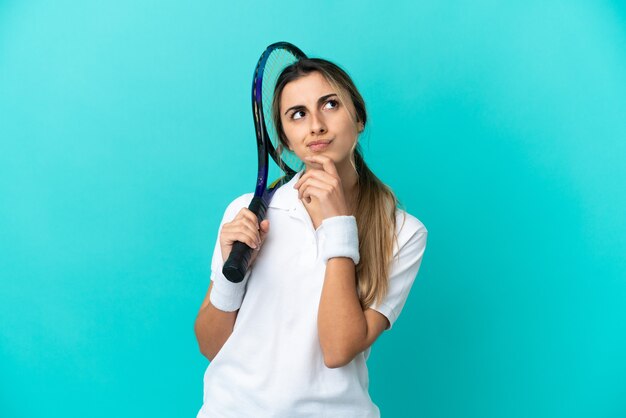 Young woman tennis player isolated on blue background and looking up