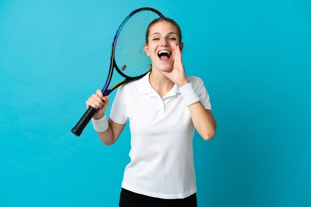 Young woman tennis player isolated on blue shouting with mouth wide open