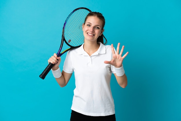 Молодая женщина-теннисистка изолирована на синей стене, считая пять пальцами