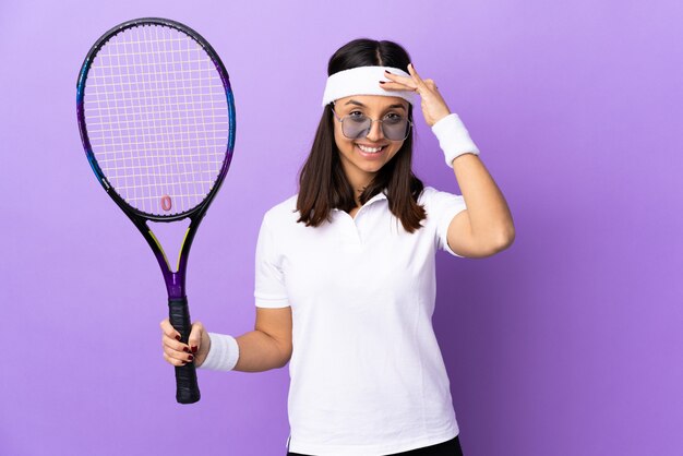 Young woman tennis player over wall saluting with hand with happy expression