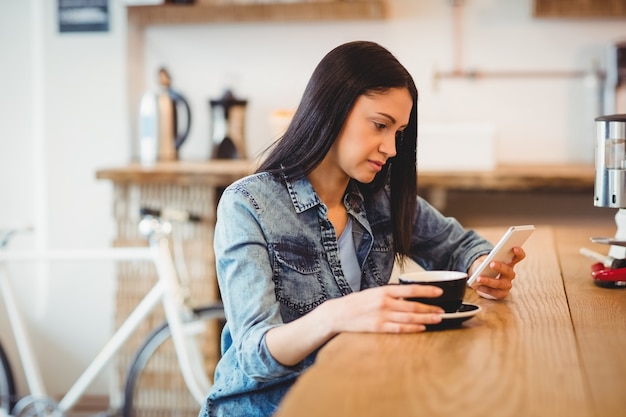 コーヒーカップを保持しながら携帯電話で若い女性のテキストメッセージング