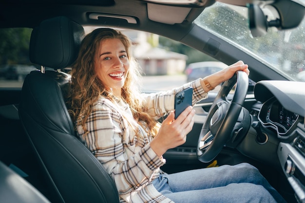 車を運転している間にスマートフォンでメッセージを送っている若い女性