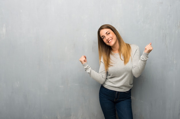 Young woman on textured wall celebrating a victory