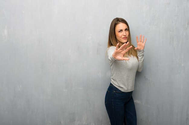 Young woman on textured wall is a little bit nervous and scared stretching hands to the front