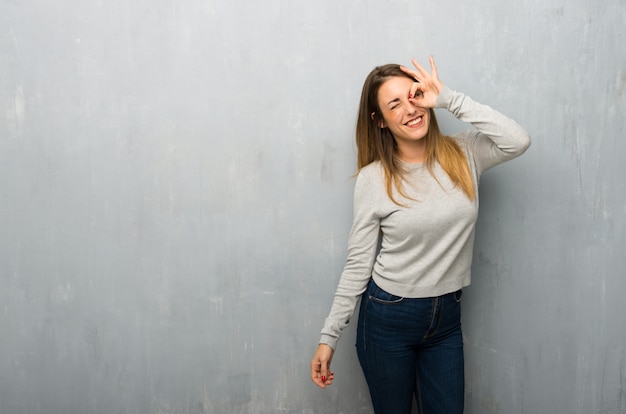 La giovane donna sulla parete strutturata fa l'emozione faccia buffa e pazza