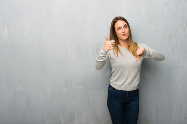 Young woman on textured wall making good-bad sign. undecided between yes or not