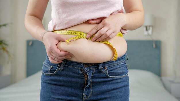 Photo young woman thinking of loosing weight measuring her waist with measuring tape concept of dieting