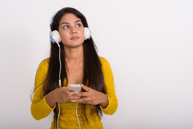 Young woman thinking while listening to music and holding mobile phone