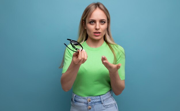 Young woman thoughtfully holding glasses with diopters on a blue background