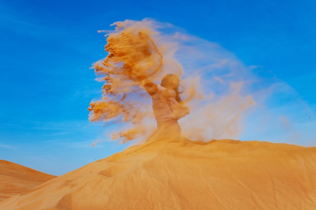 Young woman throwing sand in orande desert