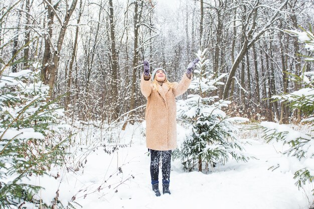 晴れた冬の日に雪を空中に投げる若い女性は、幸せで楽しいです。