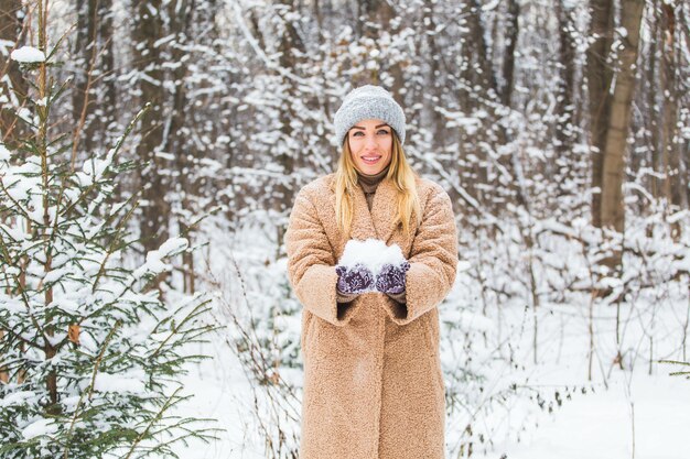 晴れた冬の日に空中に雪を投げる若い女性は、幸せで楽しいです。