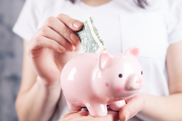 Young woman throws dollar into piggy bank