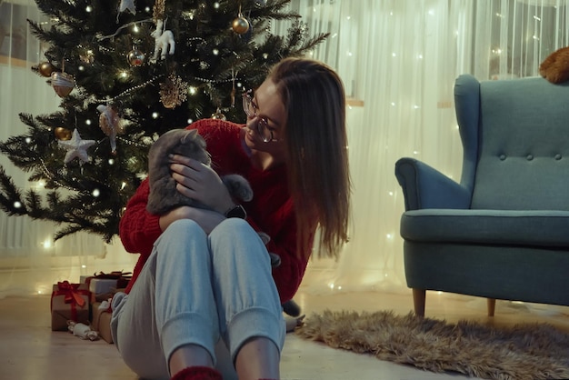 Молодая женщина вместе с котом сидит возле елки Рождество с домашним котом