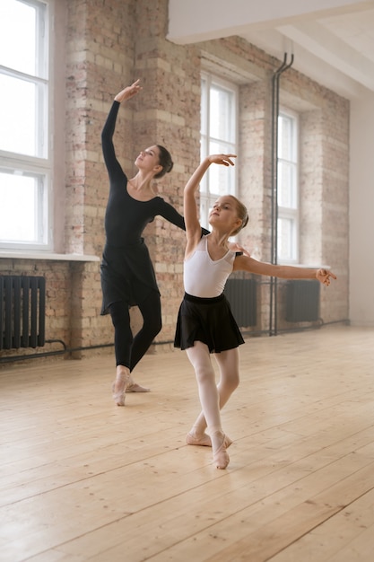 Photo young woman together with little girl dancing ballet during their training in dance studio