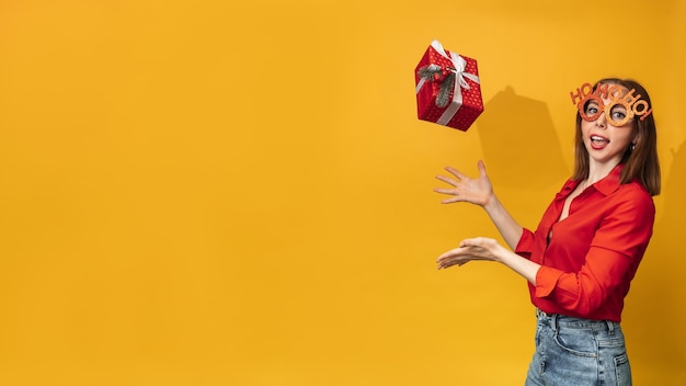 A young woman tosses a Christmas box in her hands on a yellow background The concept of celebrating Christmas and New Year A place for your text