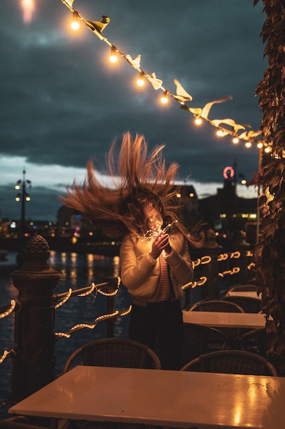 Foto giovane donna che lancia i capelli mentre tiene in mano apparecchi di illuminazione illuminata di notte