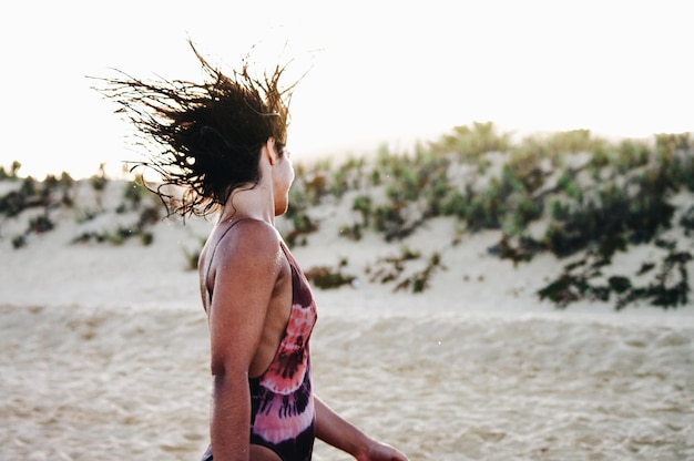 Photo young woman tossing hair while standing on sand at beach