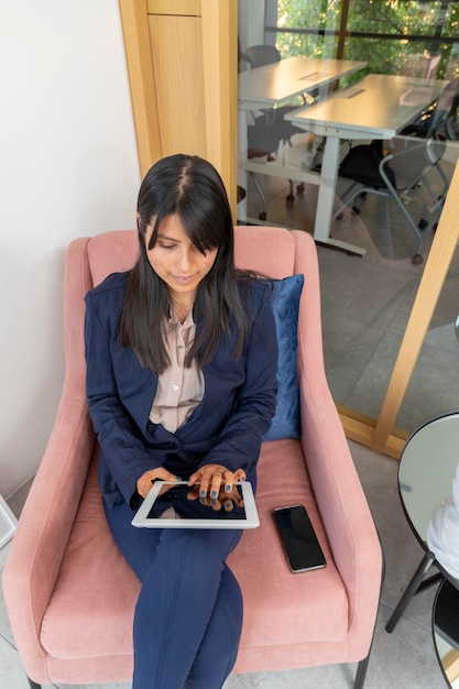 Young woman touches the screen of a digital tablet with her fingers while sitting on an armchair in the office