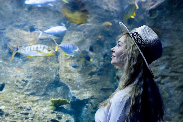 A young woman touches a stingray fish in an oceanarium tunnel